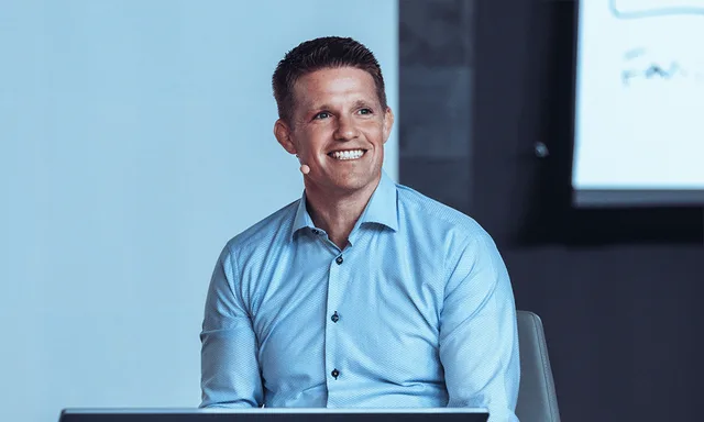Russell Brunson smiling on stage in a light blue shirt